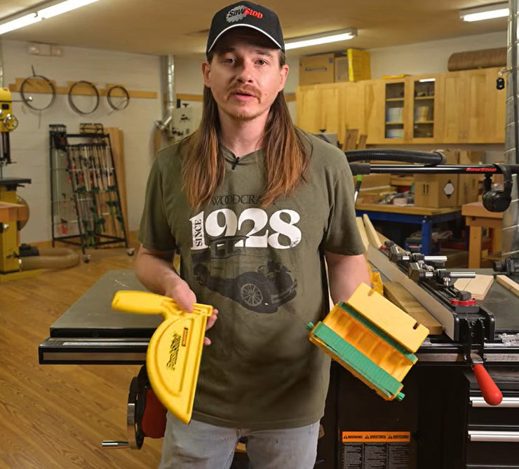 Woodworker in a workshop holding a push stick and pushblock while standing in front of a table saw.