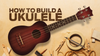 Ukulele with dark wood body and tuning pegs, surrounded by woodworking tools and materials on plywood surface