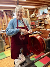 Elderly woman smiling while turning a wooden bowl on a lathe in a workshop