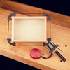 Corner band clamp securing a rectangular wooden box on a workbench for gluing or assembly.