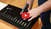 Hands adjusting a WoodRiver growth chart router jig clamped to a wooden workbench.
