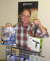 Man holding a hand saw and a clamp, standing behind woodworking tool kits and storage boxes