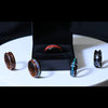 Five handcrafted rings with wood and resin inlays displayed on a white surface and black ring box.