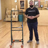 Woodworker demonstrating a metal panel cart with casters in a workshop with plywood sheets and tools.