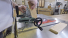 Hands guiding a tenoning jig holding a wood piece on a table saw for cutting tenons.