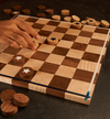 Hand placing wooden checker piece on handcrafted maple and walnut checkerboard with star inlays.