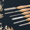 Set of five woodturning chisels with wooden handles and metal blades, surrounded by wood shavings on a dark surface.