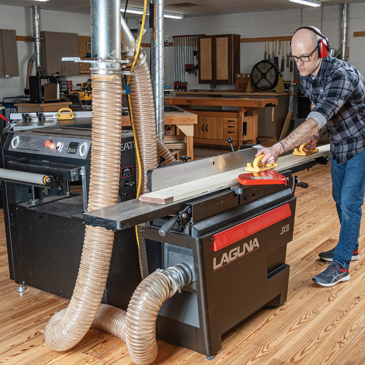 Woodworker using a floor-standing jointer in a shop, with a stationary planer in view.