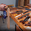 Hands using a backsaw to cut dovetail joints on a clamped wooden board with various saws on the workbench.