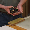 Hands holding a block plane blade being prepared for sharpening next to a whetstone.