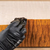 Gloved hand applying amber dye stain to curly maple wood with cloth rag