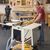 A beginner woodworker ripping a board on a hybrid table saw in a woodshop.